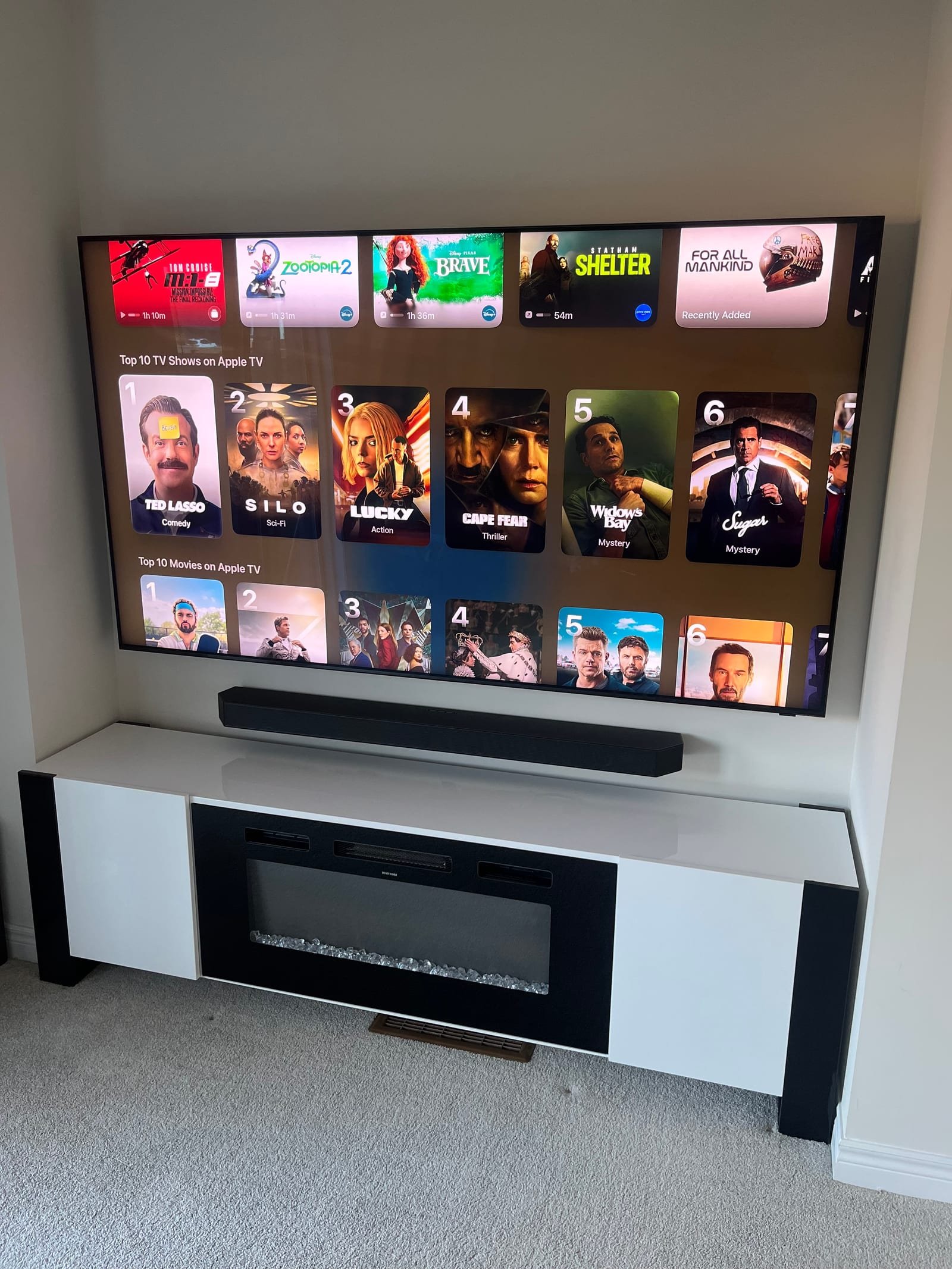 Wall-mounted television above an electric fireplace with a soundbar